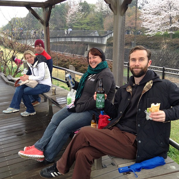 Greg, Amanda, Melissa, and Dan sit on a park bench, drinking beer and eating sandwiches.