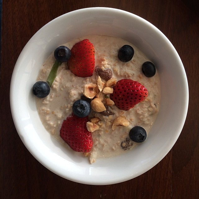 A bowl of oatmeal is topped with strawberries, blueberries, and nuts.