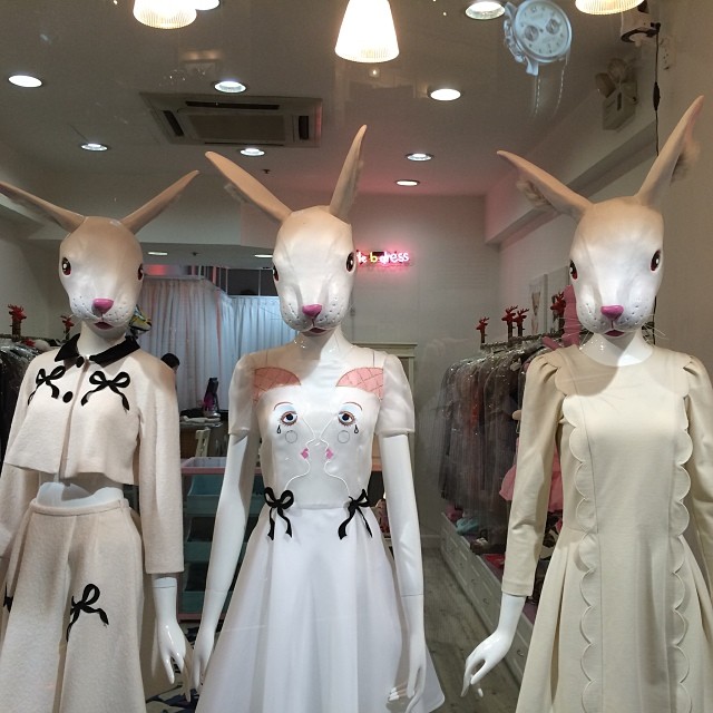 Three mannequins wearing women’s clothing for sale stand in a shop window. The mannequins inexplicably have the heads of rabbits.