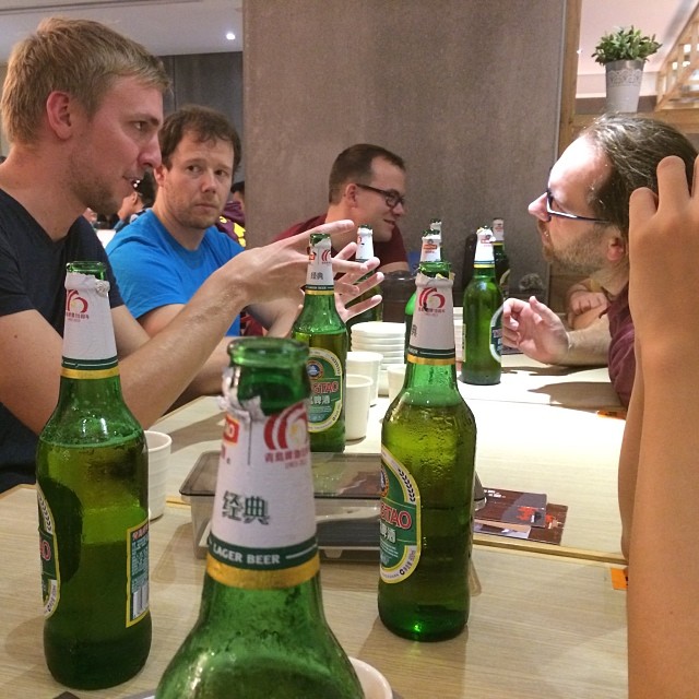Many empty bottles of Tsingtao beer clutter up a restaurant table, around which several young men sit.