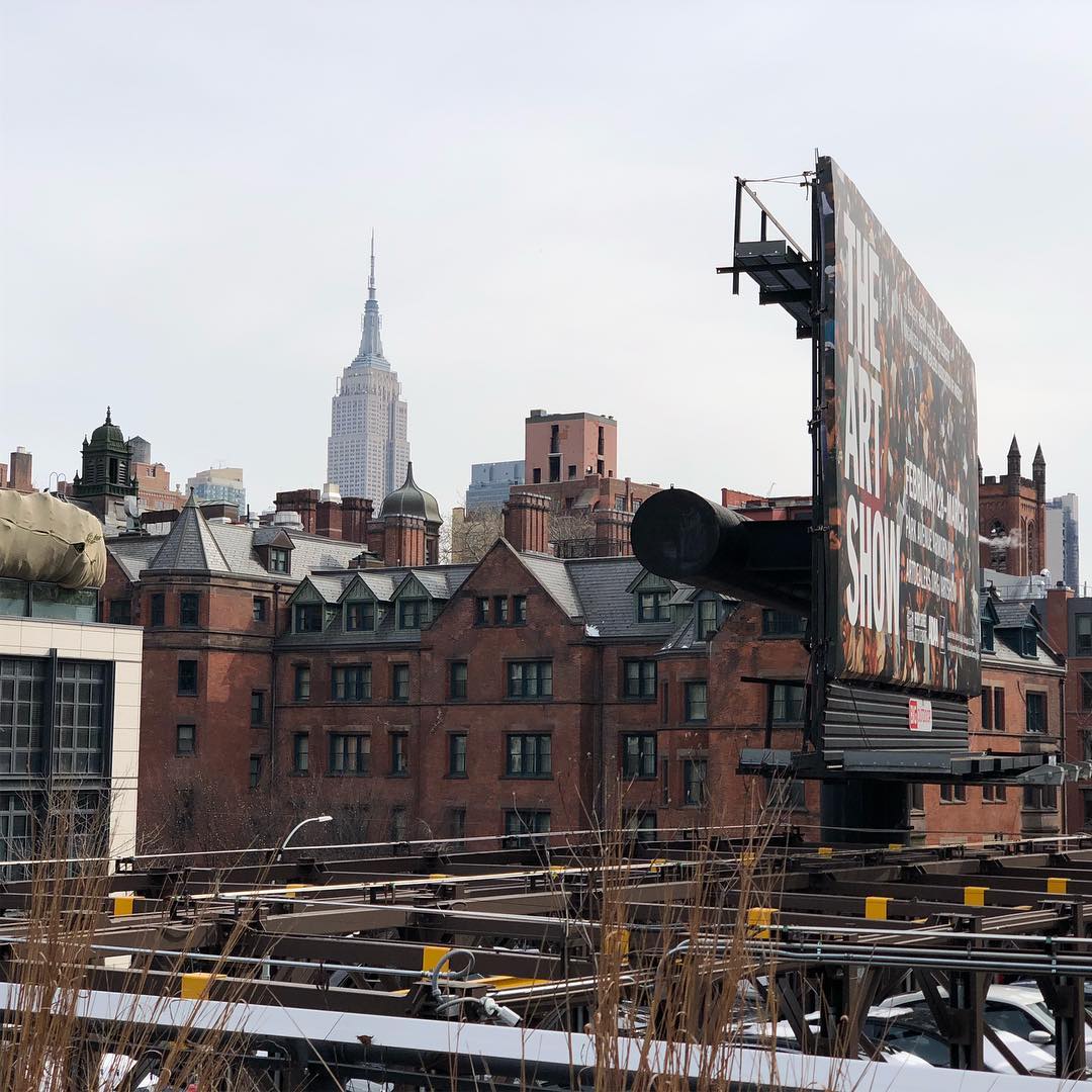 Manhattan under a gray sky. The Empire State Building is visible over the mass of brick buildings closer to the camera.