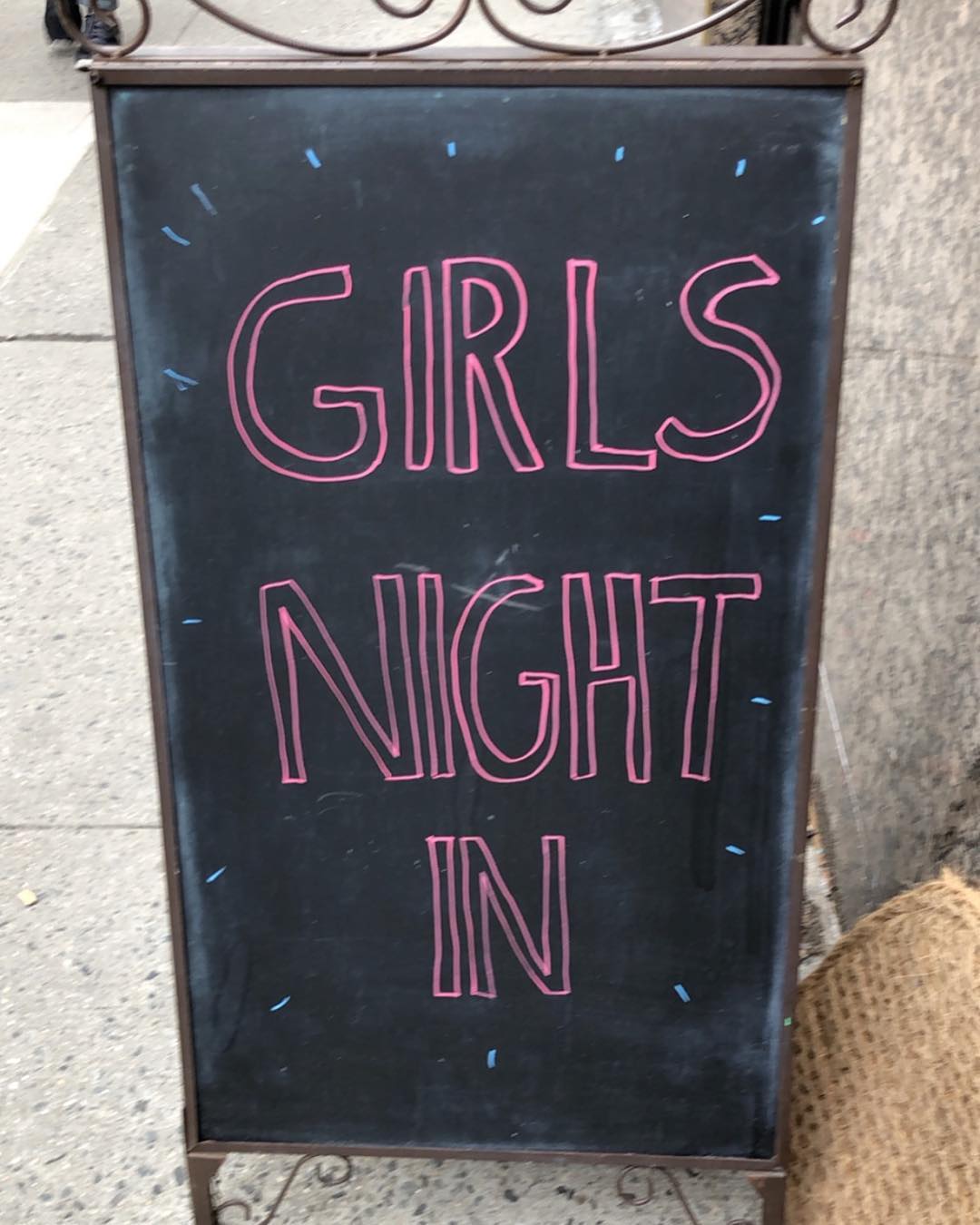 “GIRLS NIGHT IN” is written in pink on a folding sidewalk chalkboard.