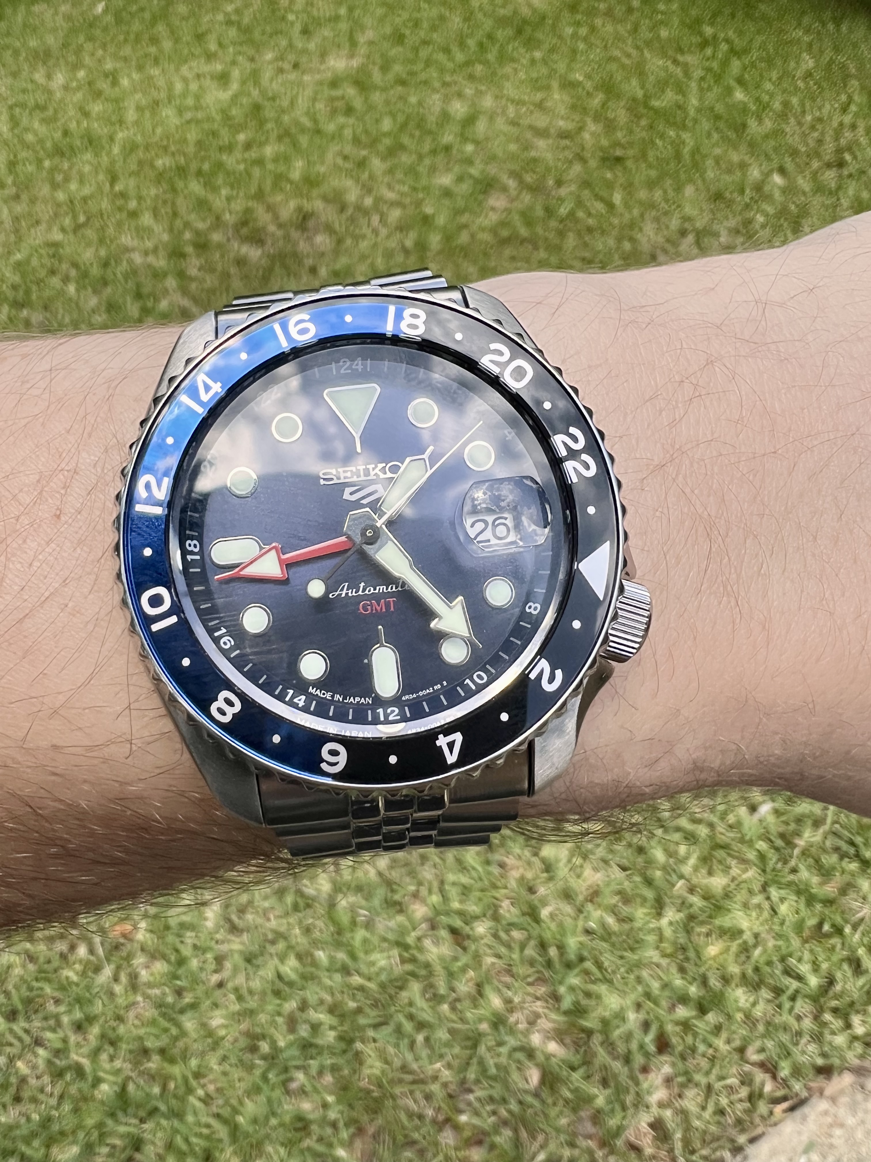 wristshot of a blue dial Seiko 5 GMT watch, taken in jae's backyard