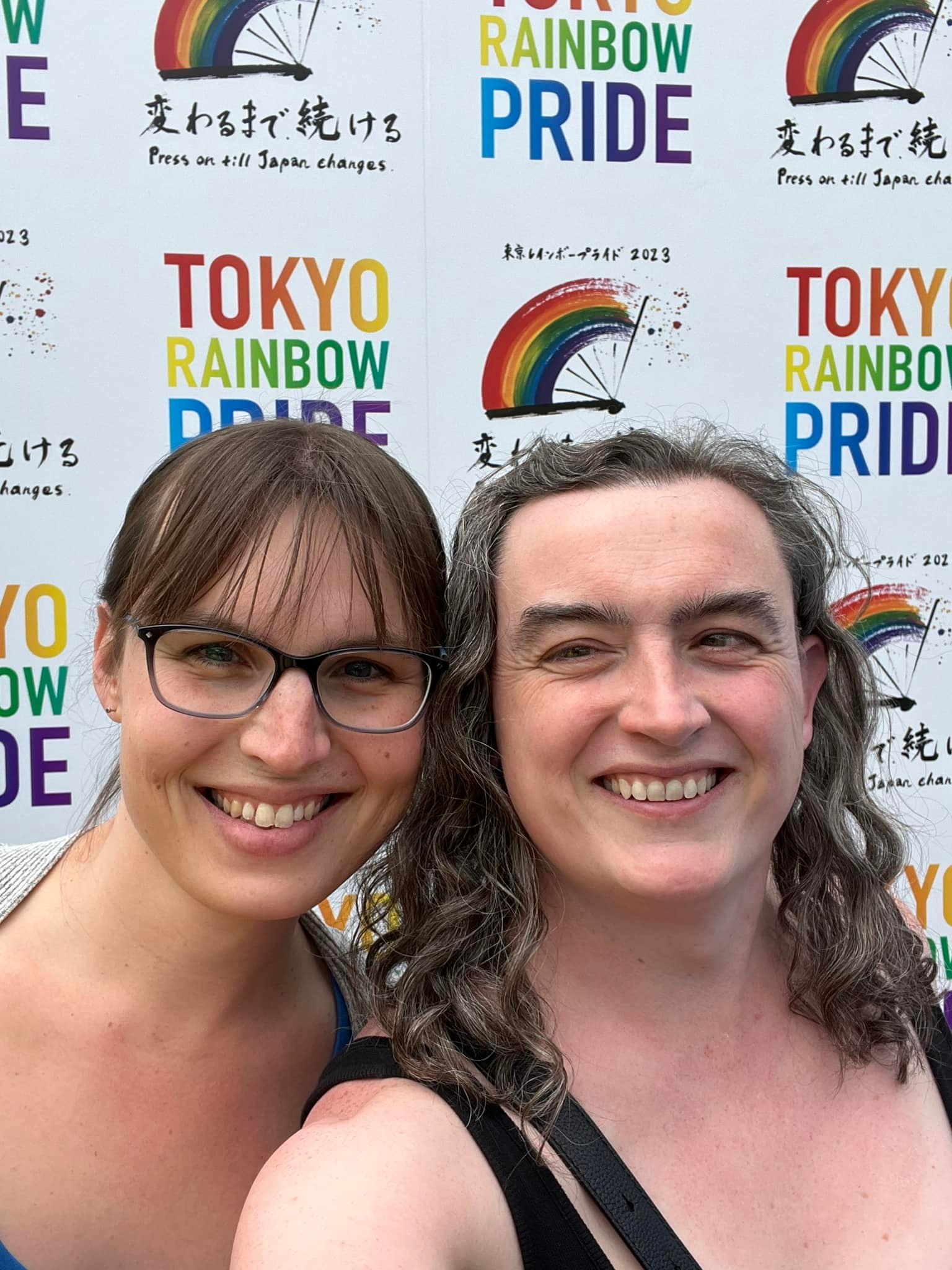 A selfie of two smiling girls. They’re standing in front of a wall which reads “TOKYO RAINBOW PRIDE”.