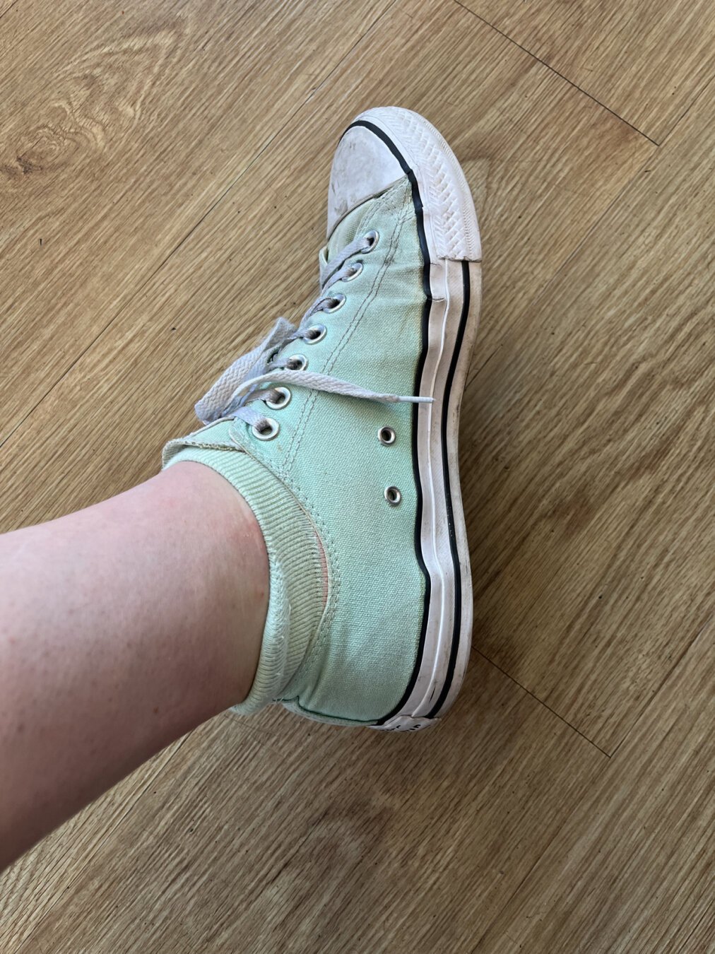 A foot. The foot is wearing a mint green sock and a mint green shoe—Converse Chuck Taylor All-Stars.