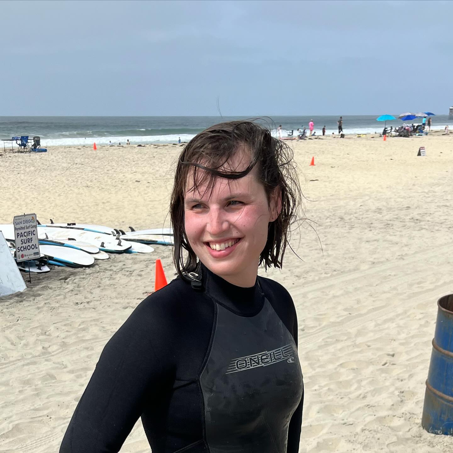 Eryn stands on a beach in a wetsuit.
Her hair is wet and plastered to her head in a way that suggests recent activity in the ocean behind her.