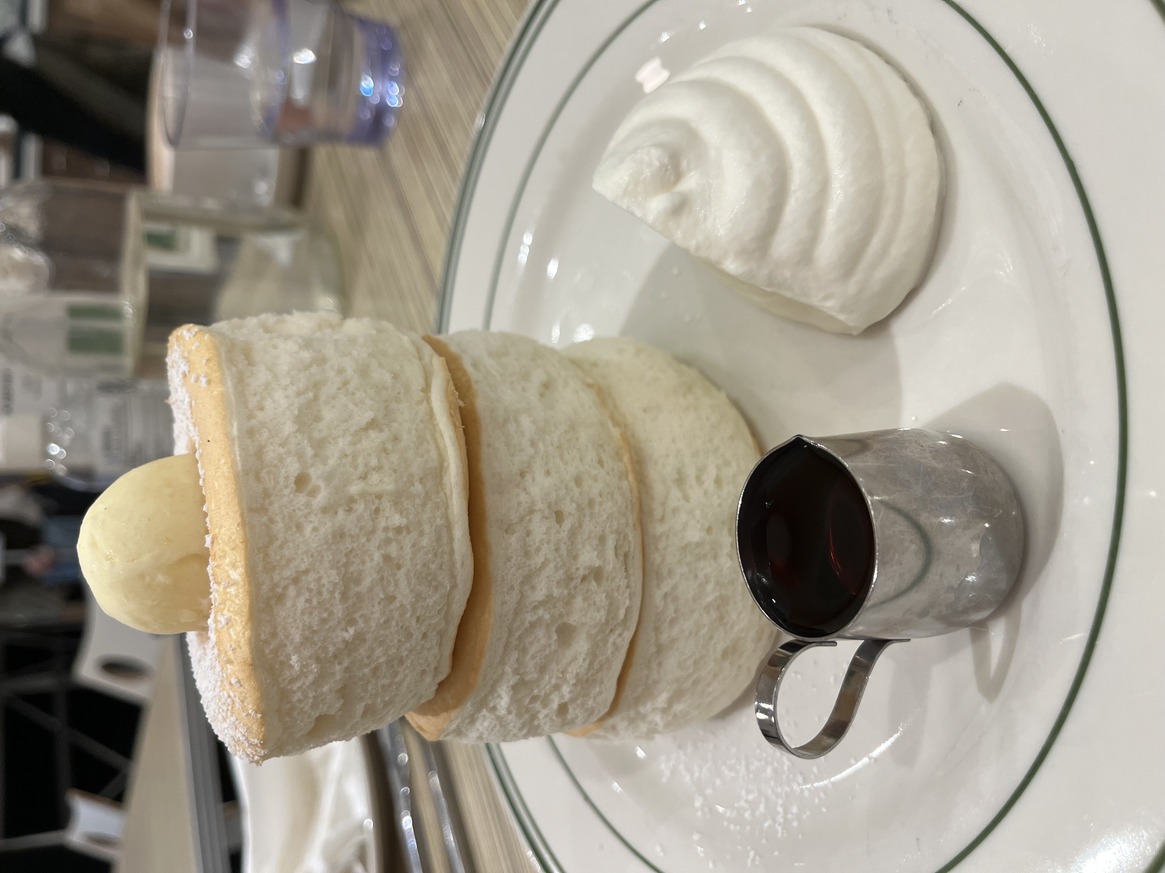 Three incredibly thick, wobbly pancakes are precariously
stacked on a plate. There’s a hemisphere of butter on top of the stack,
a dollop of whipped creme next to the stack, and a small pot of maple
syrup in front of it.