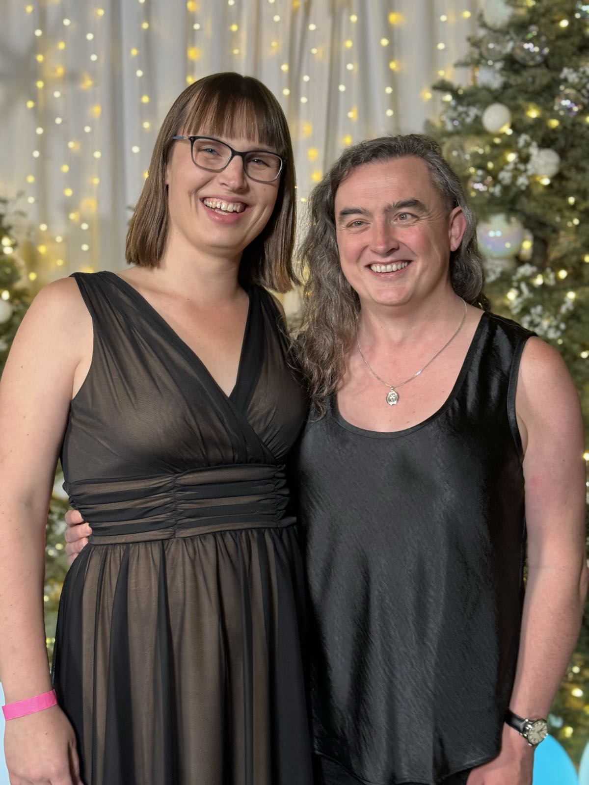 Eryn and I are standing next to each other in front of a Christmas tree and wall of twinkling lights.
She’s in a fancy, dark-colored dress.
I’m in a black blouse and matching pants.
She’s laughing and my smile doesn’t looked forced, which is pretty good for me.