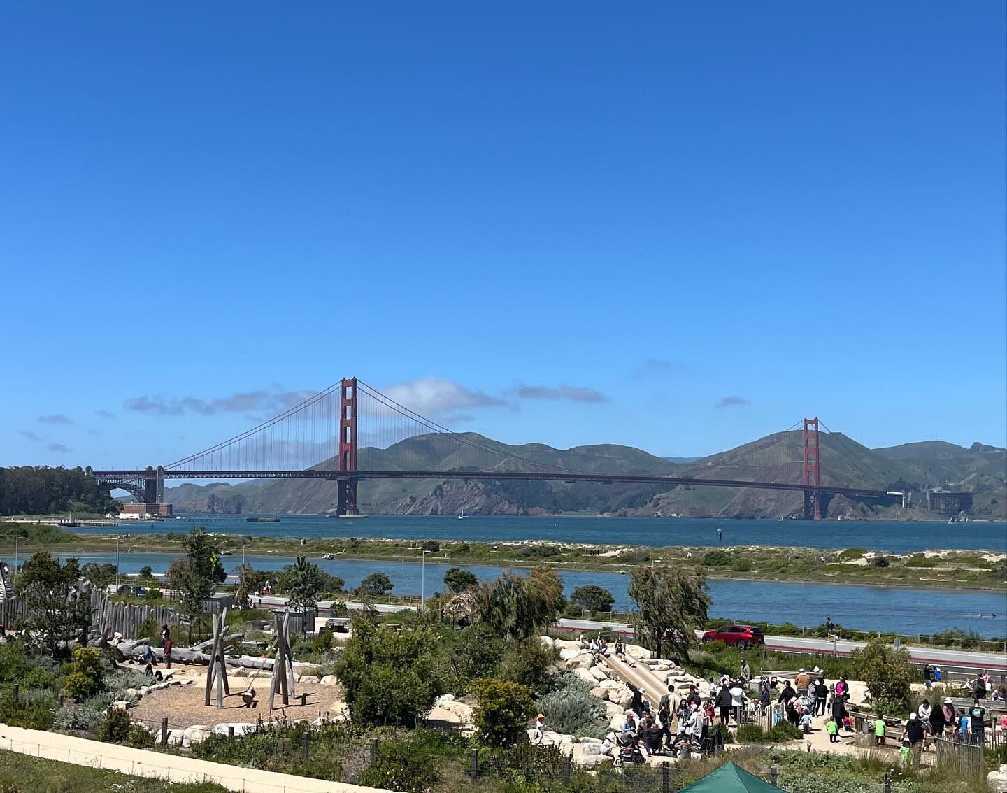 The Golden Gate Bridge spans the opening of San Francisco Bay on a sunny, clear day. The photo is from the San Francisco side, so the Marin headlands are visible on the other side of the bridge. On the near side some of the playground at Tunnel Tops park is visible.