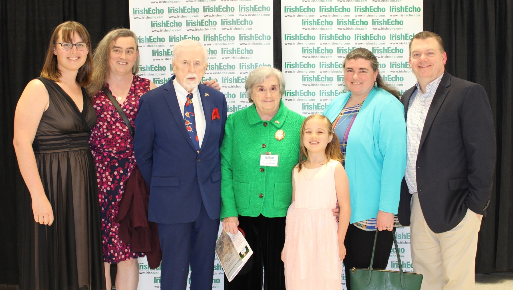 A photo of my family at the Heroes of Irish America awards ceremony.
My mom is in the center.
She has a bright green jacket on, and is wearing a nametag that identifies her as one of the award recipients.
To her left is my dad, looking very dapper in a blue suit.
I’m to his left, in a black, red, and pink floral dress.
    Eryn is on my left, looking extremely pretty in a dark, shimmery dress.
Immediately to my mom’s right is my daughter Erin in a light pink dress.
To her right, my sister Kathleen and her husband Shawn complete the family.