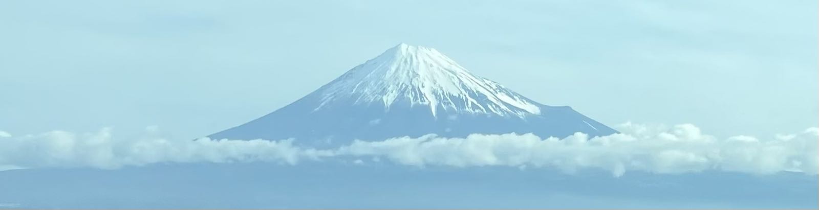 Mount Fuji, as seen from a passing bullet train. The mountain is under a clear sky, though there is a layer of clouds that bisects the mountain a bit below the snow line.