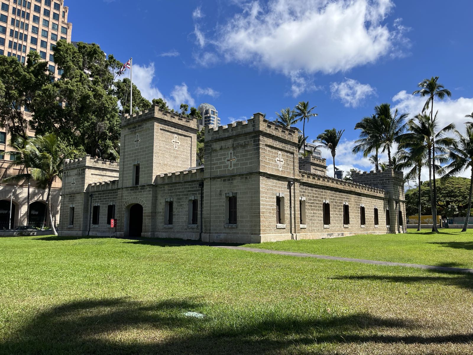 The barracks at ʻIolani Palace.
The short, single-storey building appears to be based on a European castle.
The Hawaiian flag hangs from its flag pole.