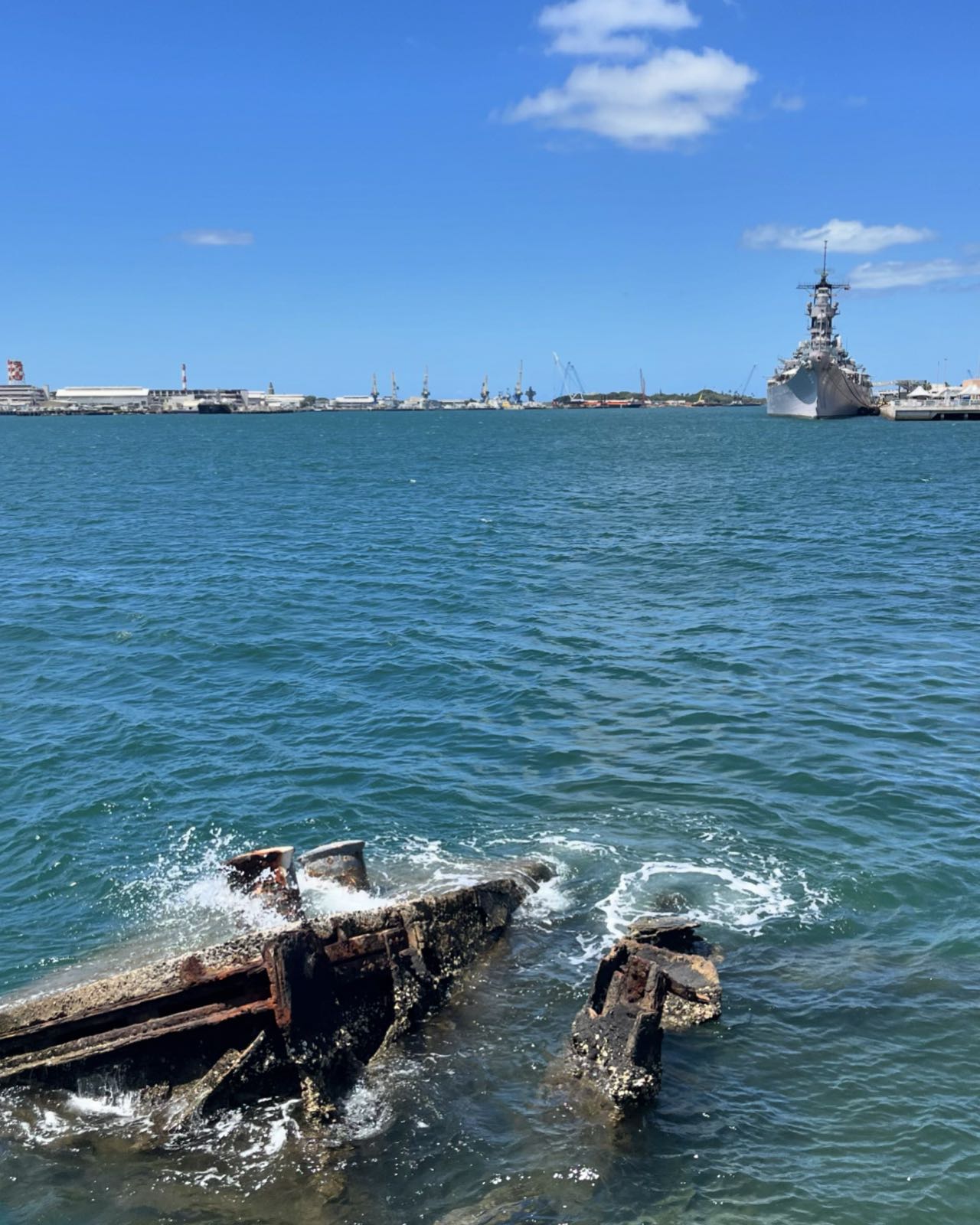 The USS Missouri (BB-63) floats in the waters of Pearl Harbor, as seen from the Arizona Memorial.
In the foreground, some rusted parts of the Arizona stick out of the water.