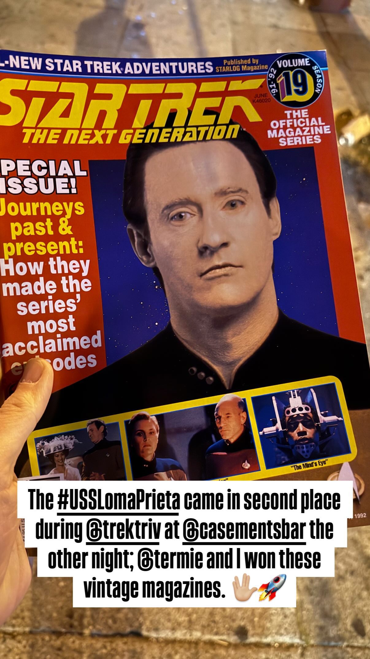 A vintage magazine is being held up to the camera. Behind the magazine, a sidewalk is visible. It’s an issue of “Star Trek: The Next Generation” magazine, dated 1992. A caption near the bottom reads “The #USSLomaPrieta came in second place during @trektriv at @casementsbar the other night; @termie and I won these vintage magazines. 🖖🏼🚀”