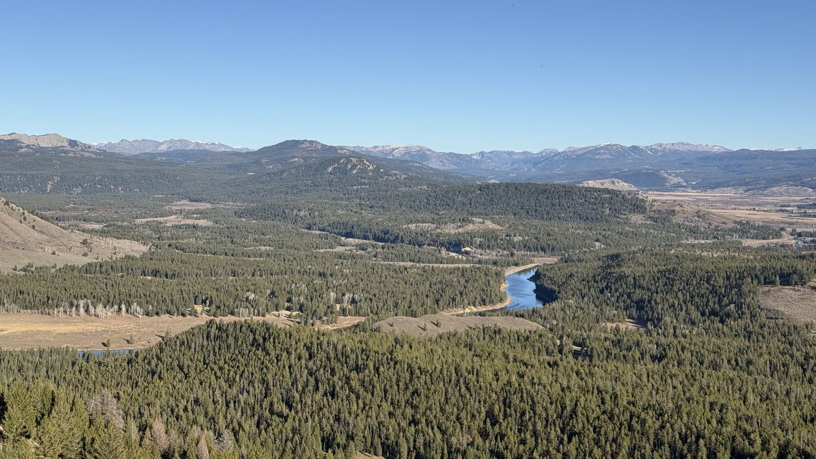 A wooded valley lies between mountains. A blue river snakes through the trees in the center of the frame.