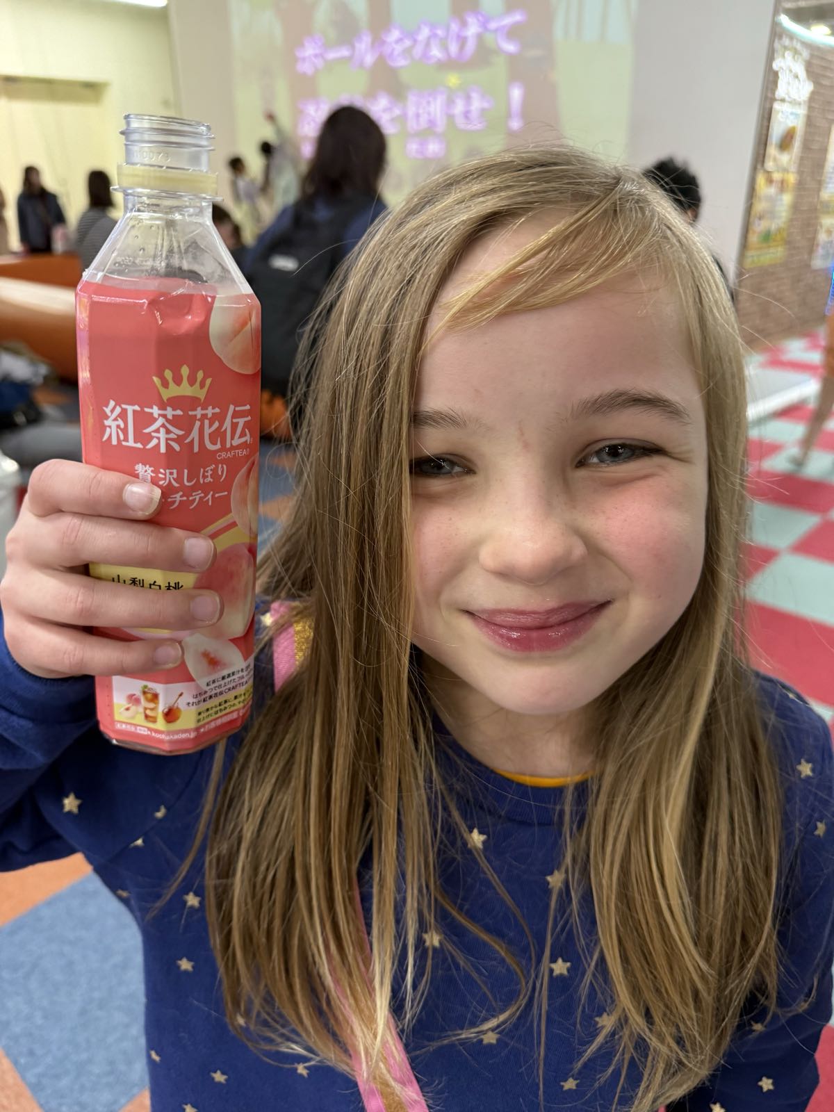A smiling girl holds a bottle of flavored iced tea next to her head.