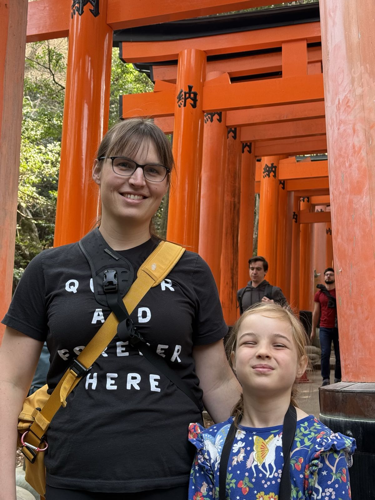 A woman and a child pose for a photo at the end of a tunnel made of many vermilion torii gates.