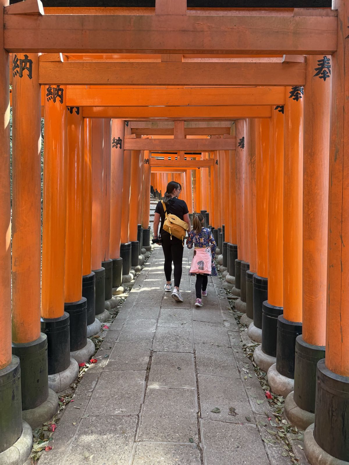 A woman and a child walk away from the camera, down a tunnel of vermilion torii gates.