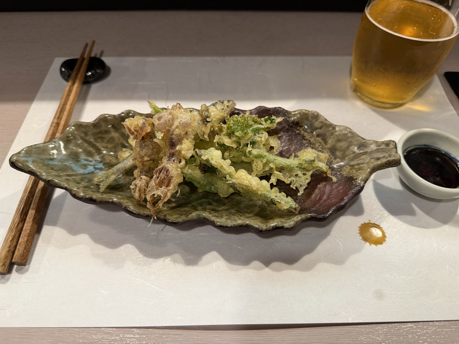 On a plate shaped like a leaf sit a bunch of veggie and fish tempura.