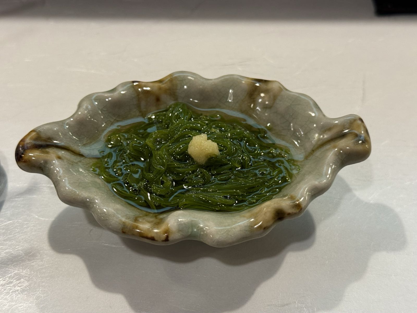 A seaweed salad sits in a small bowl that has been made to look like an oyster shell.