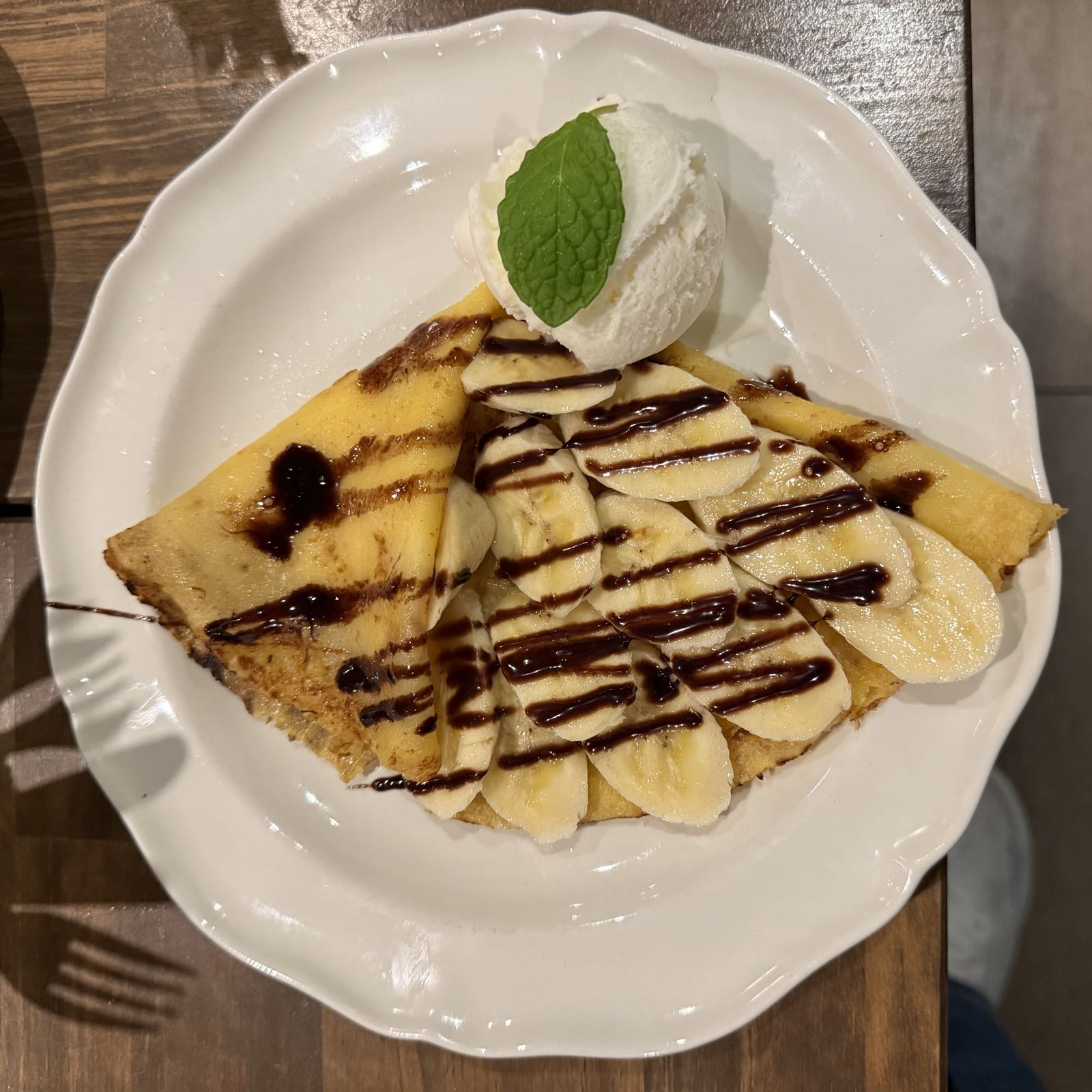 A crepe topped with banana slices and chocolate sauce has been folded and arranged to look like a fish.
