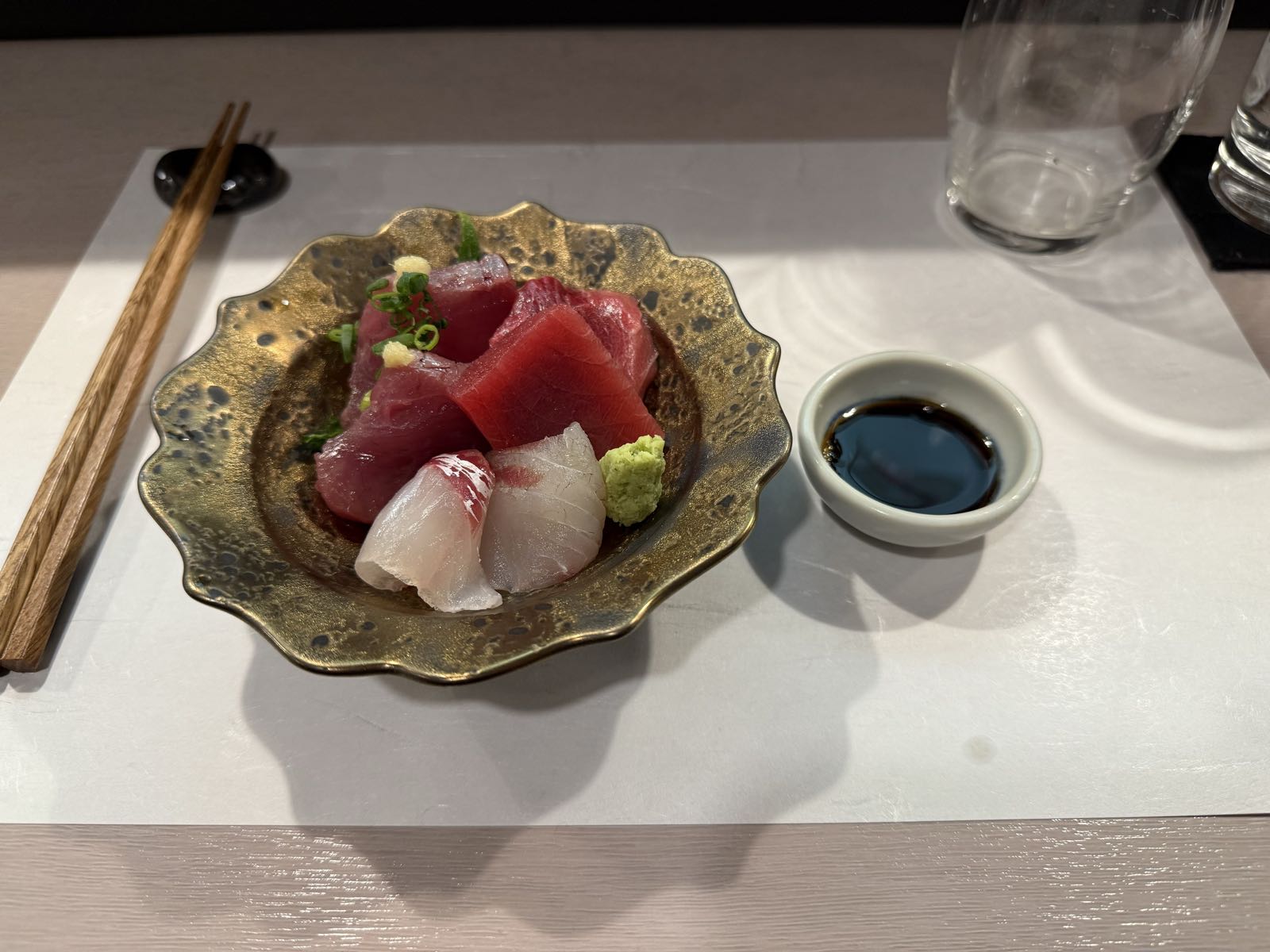 Several pieces of sashimi sit on a plate. There is also a pair of chopsticks and a small bowl for dipping.