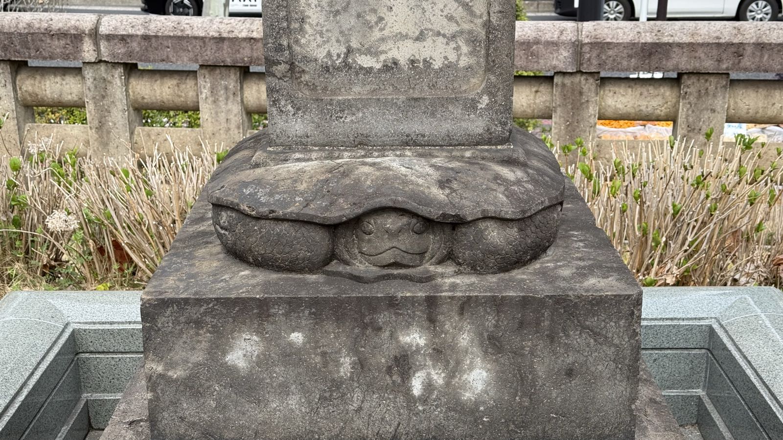 Stacked between two sections of a gravestone is a stone carving of a frog.