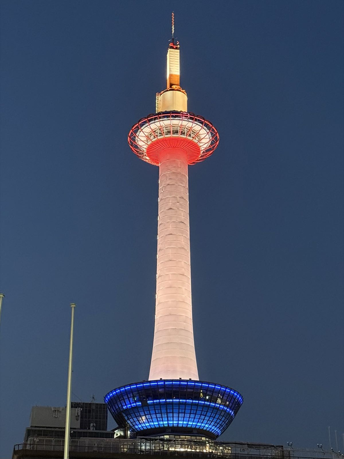 A modern looking tower is white, with a windowed section at the top lit up in red and a similar section at the bottom lit up in blue.