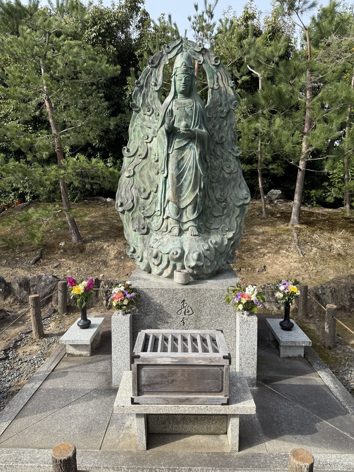 A statue of a Buddhist priest stands on a pedestal. There’s a small box for offerings in front of the pedestal.