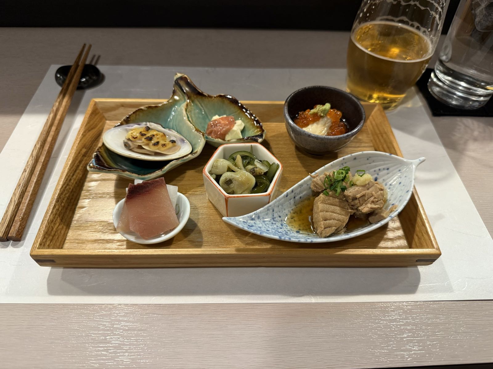 A tray has a half a dozen plates and bowls on it, each holding a different bit of food. There are some pieces of fish, some vegetables, and a number of harder-to-identify bits of food.