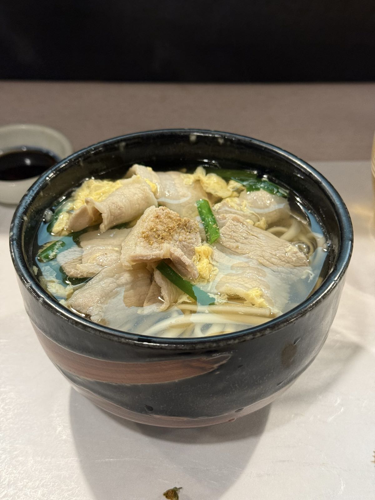 A bowl of egg-and-noodle soup appears to have some kind of meat in it.