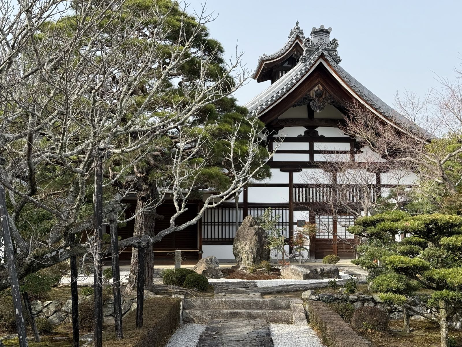 A white-and-dark-wood traditional Japanese building stands in front of some trees and a courtyard.