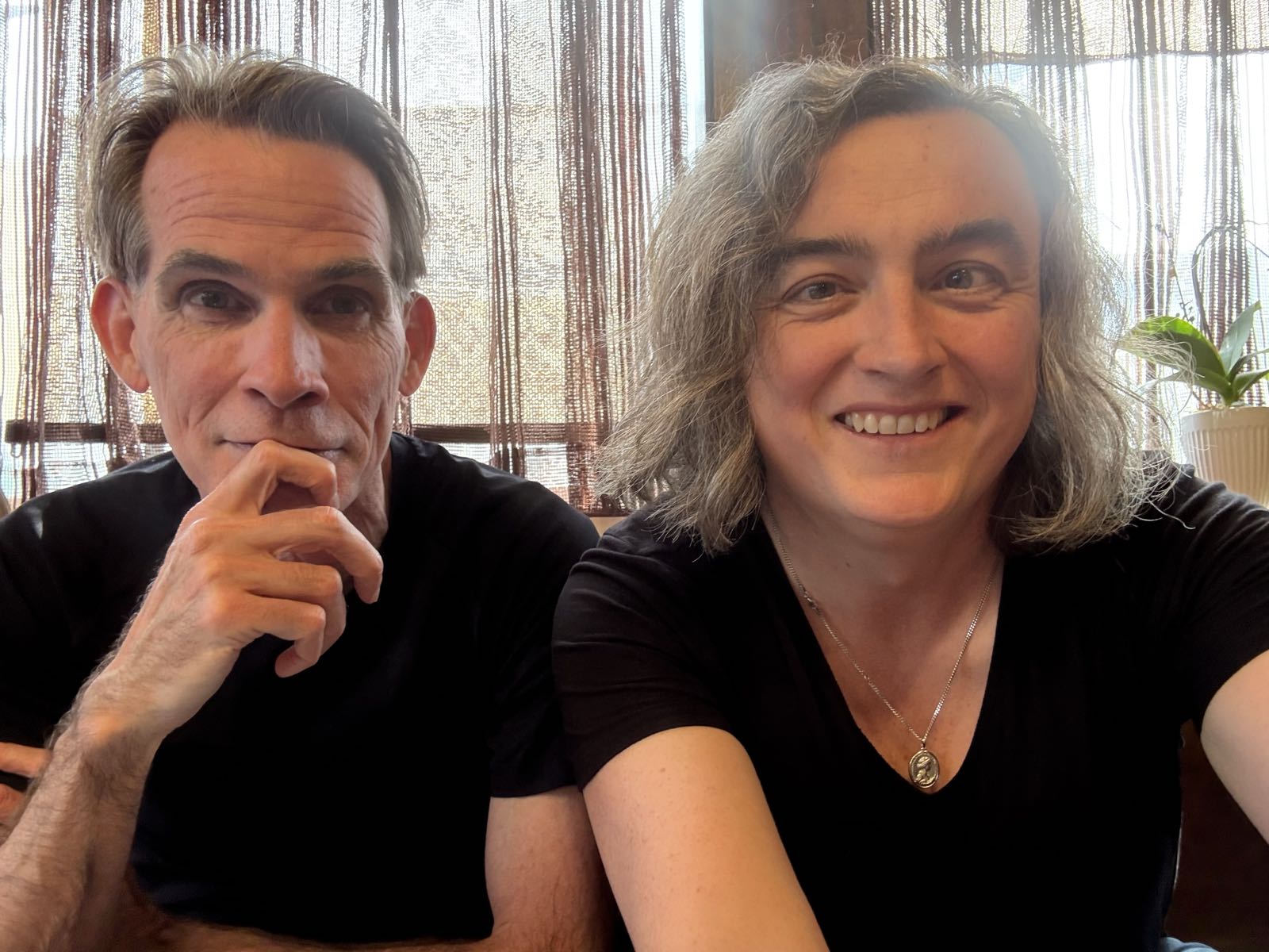 Two middle-aged people are sitting next to each other. They’re both smiling at the camera.