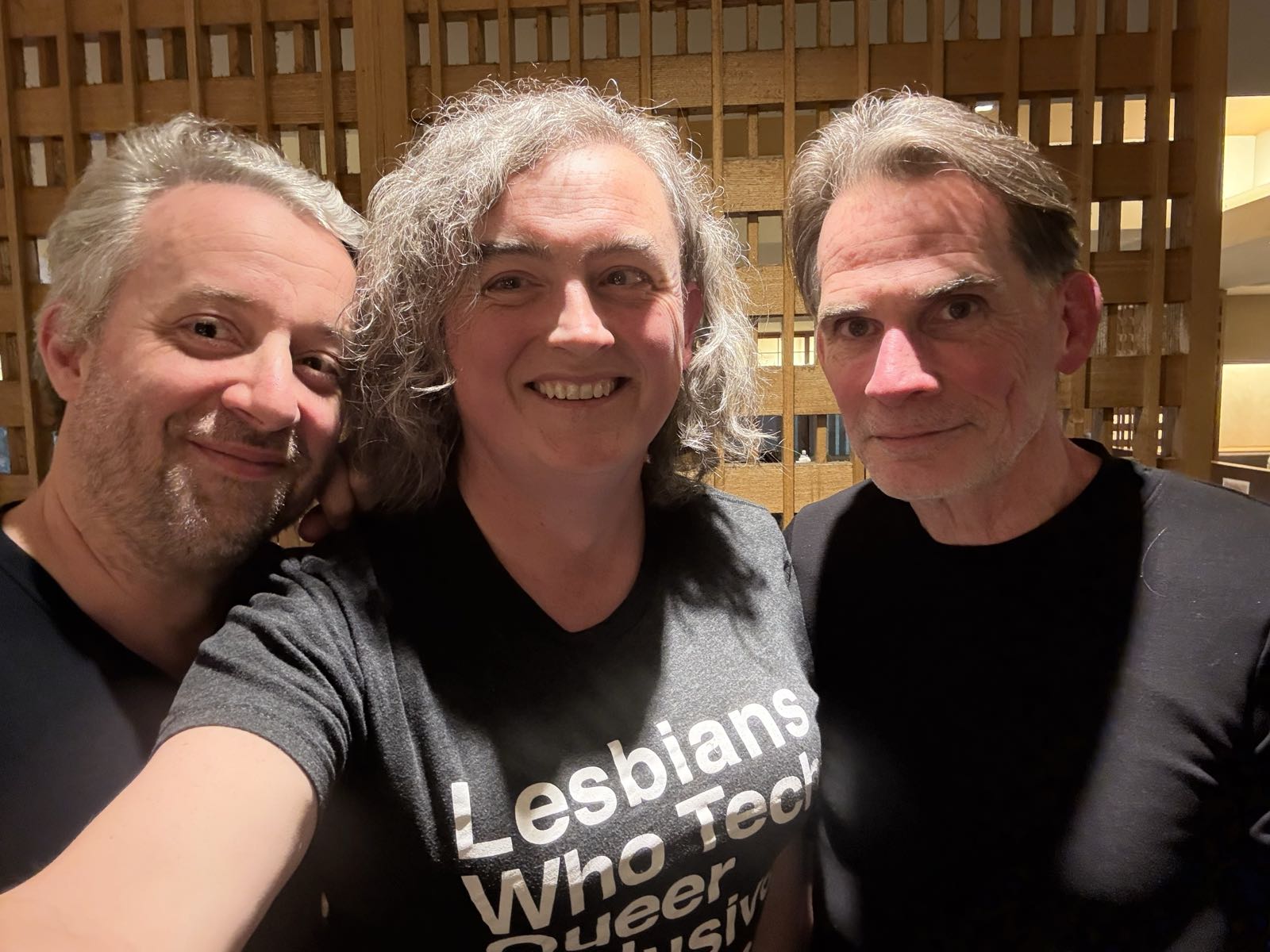 Three middle-aged adults, all in black t-shirts, pose for a selfie together. All are going gray.