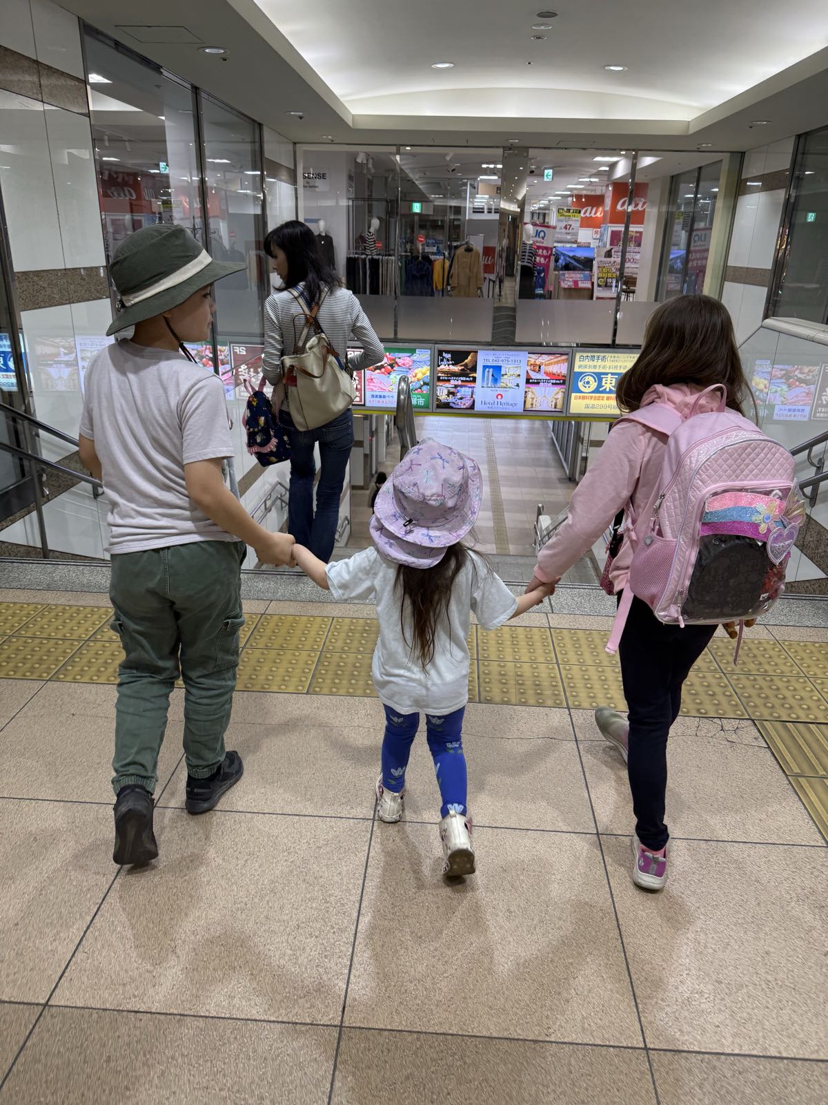 Three children hold hands as they approach the top of a stairway. The youngest child is in the middle.