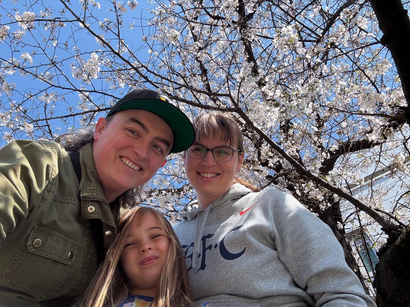 Two women and a child pose in front of a cherry tree. They’re all smiling.