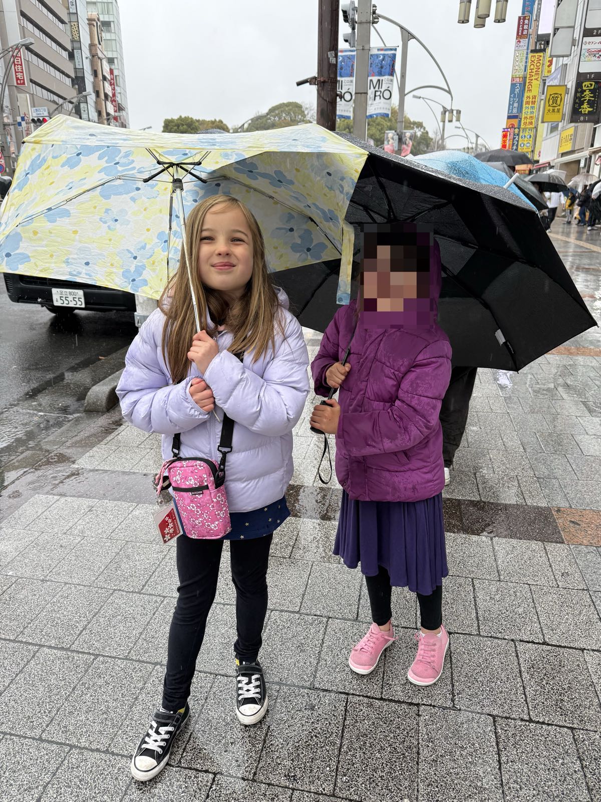 Two children stand on a sidewalk. Each is holding an umbrella.