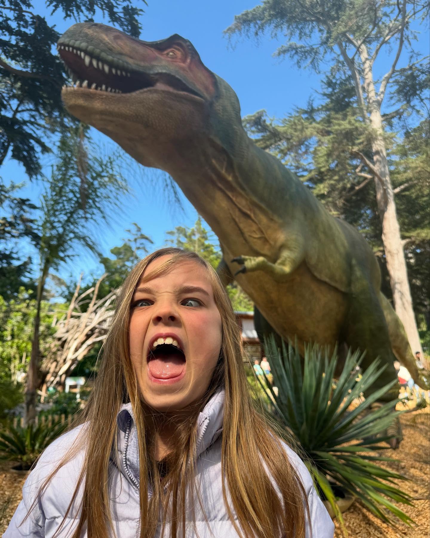 A girl makes a fierce face while standing in front of a T-rex