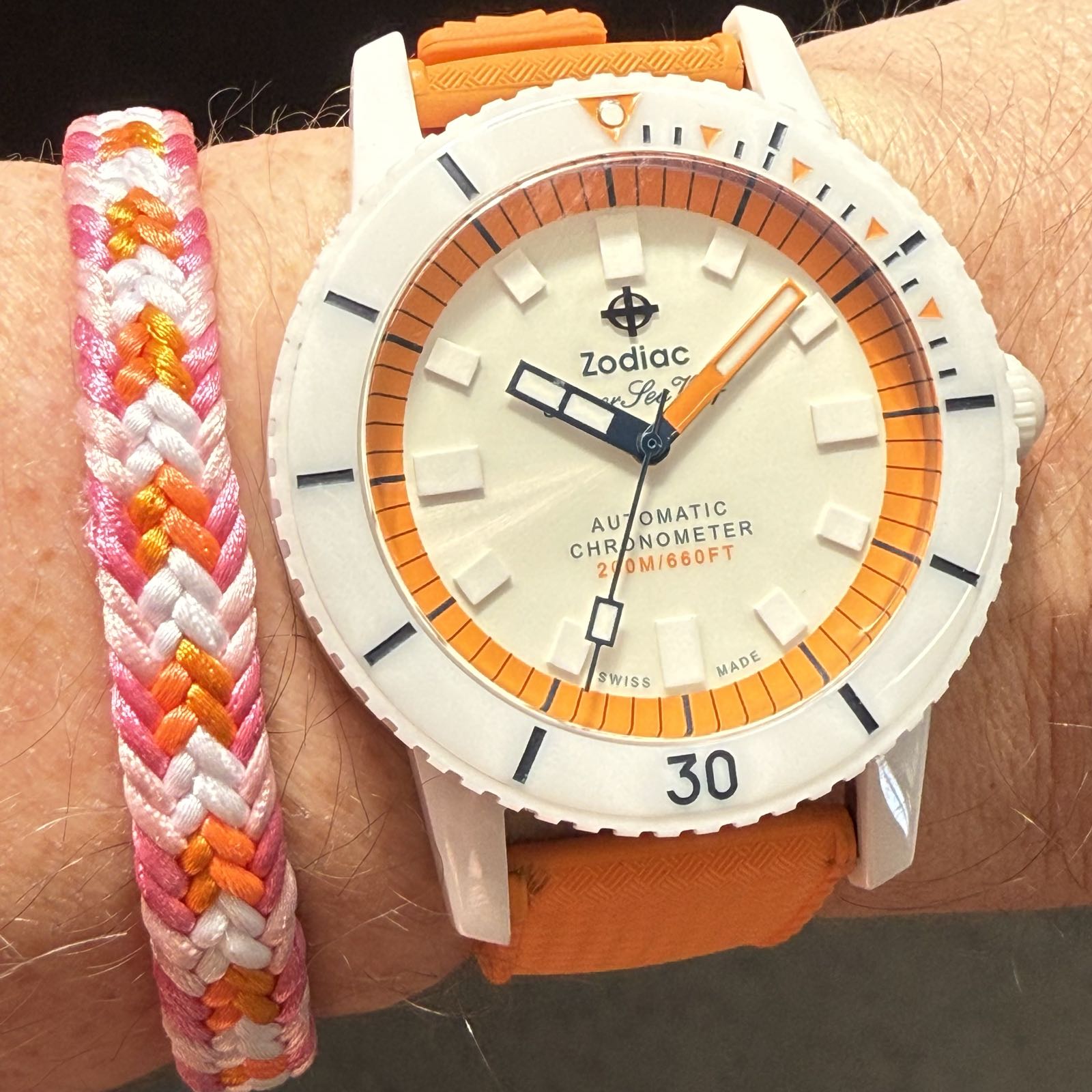 A white ceramic watch on an orange rubber strap. Various small details of the watch are in the same orange as the strap.