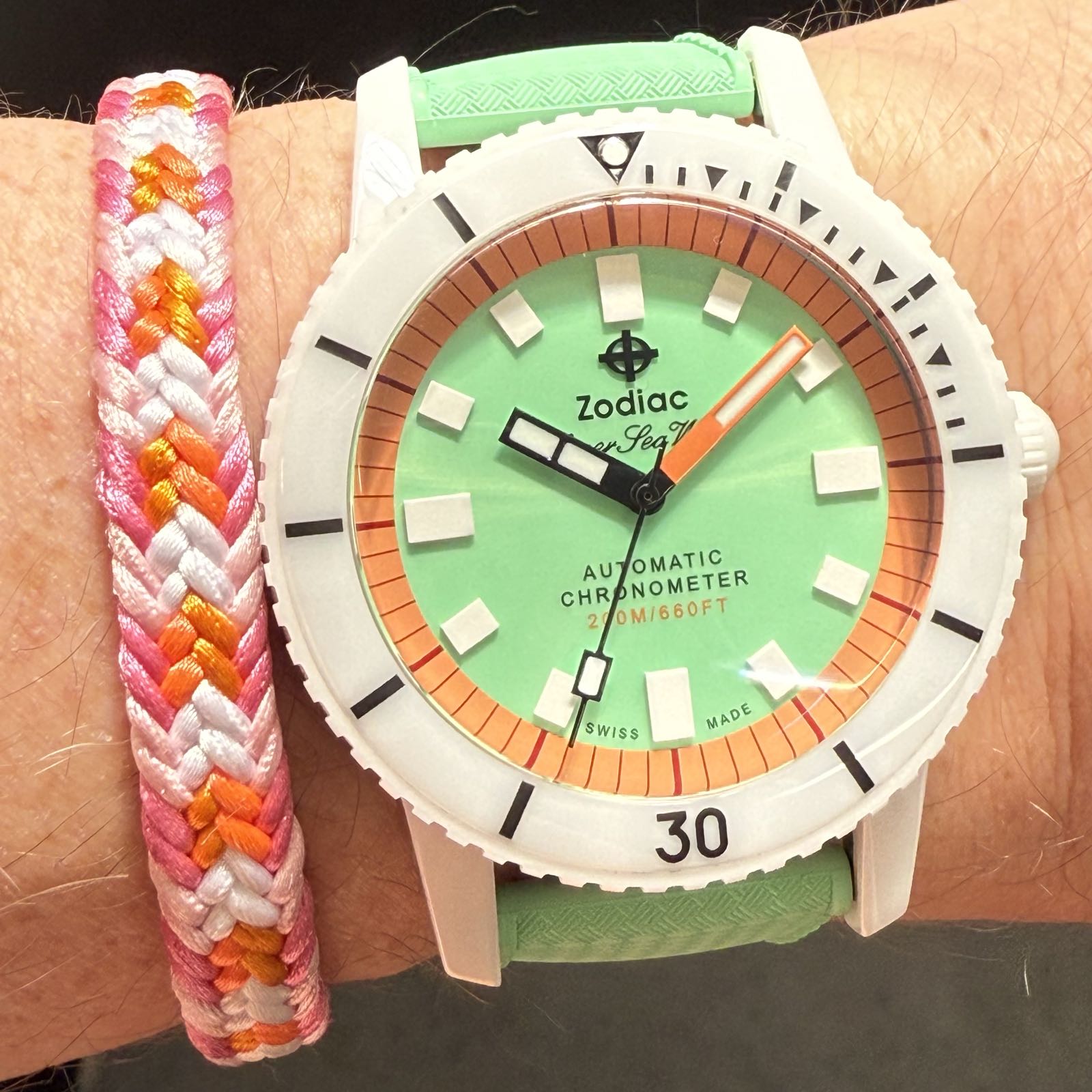 A white ceramic strap has a green dial and a matching green rubber strap. The chapter ring and minutes hand are orange.
