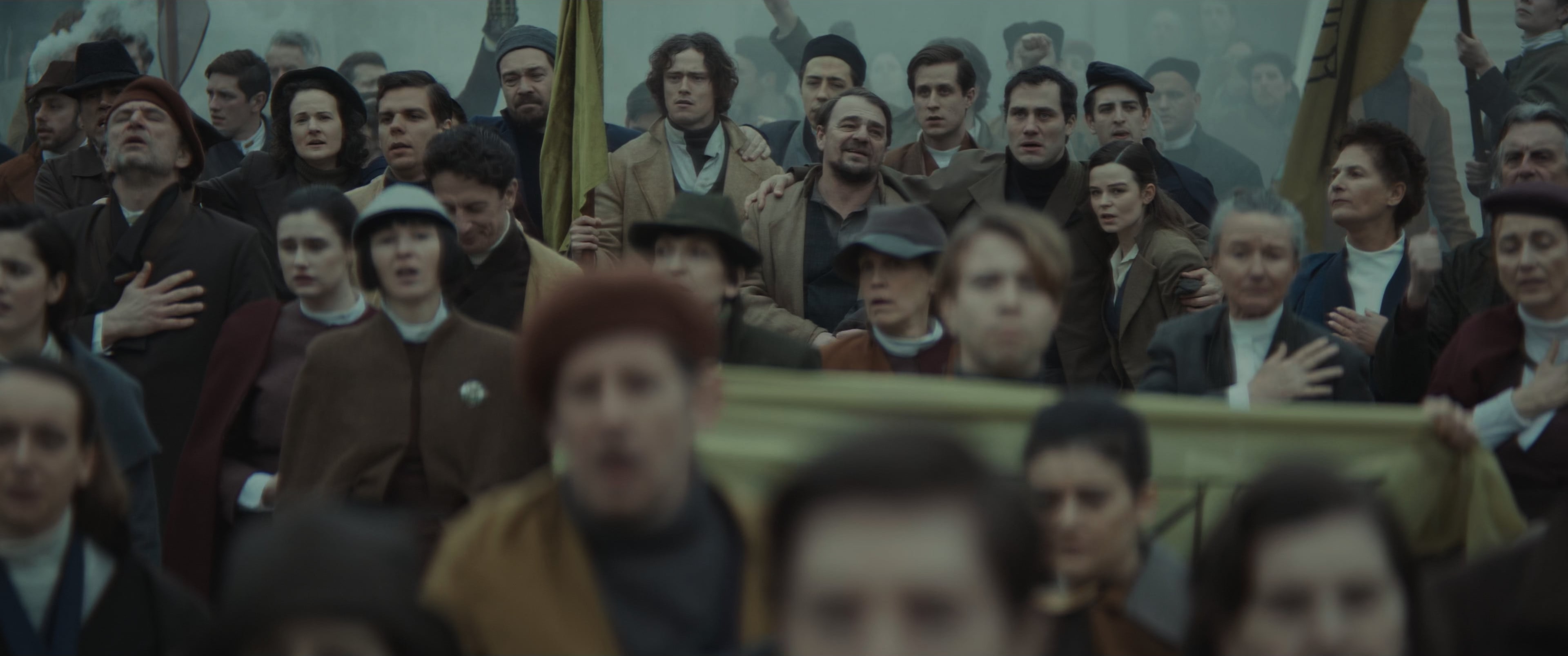 A crowd of people stand at a protest. Many appear to be singing.