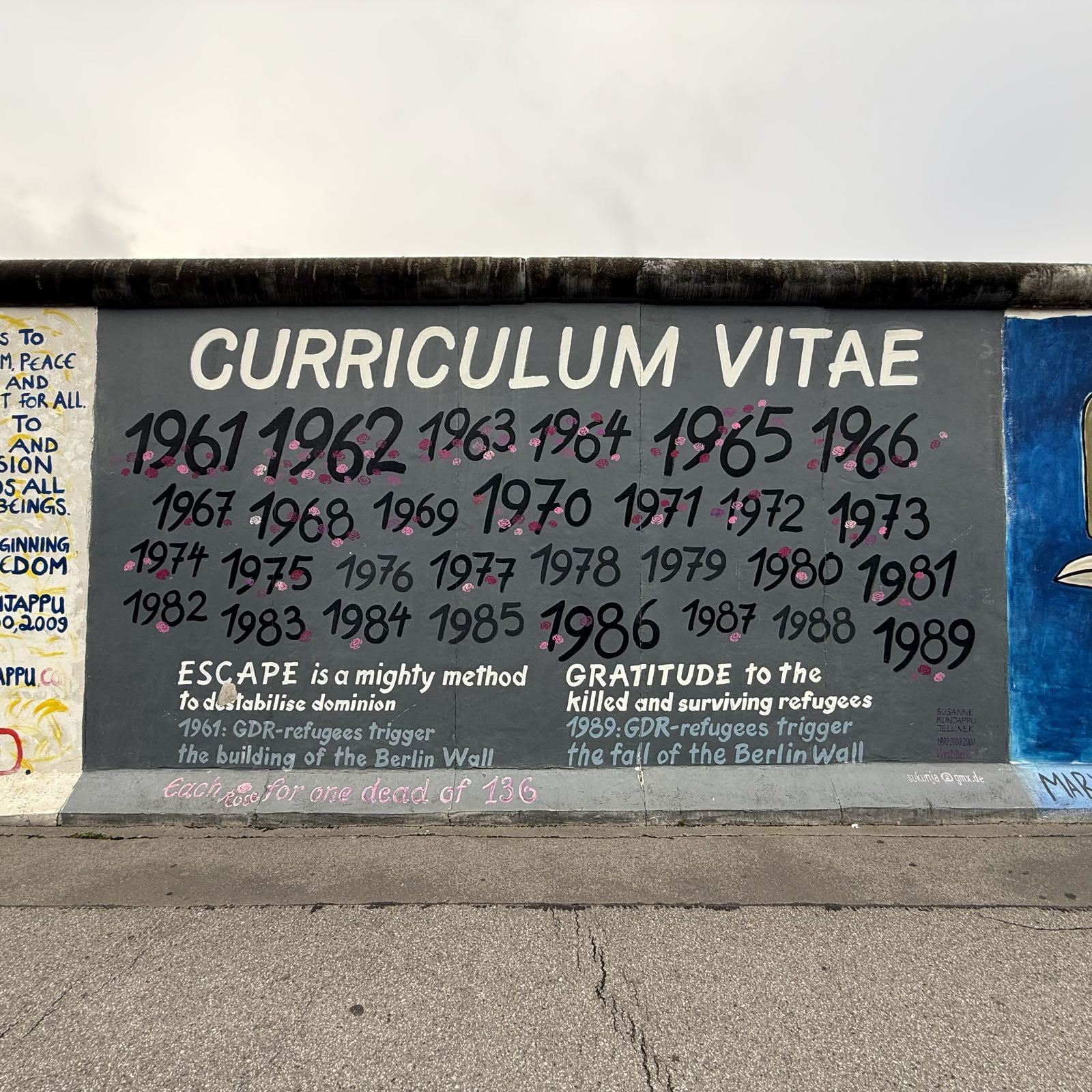 A portion of a wall is painted gray. In the gray portion, each year of the division of Berlin is listed, and each is decorated with a rose for each death of someone trying to cross the Berlin Wall.