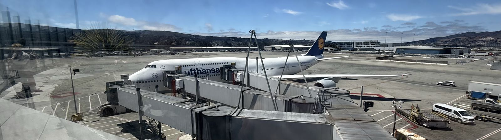 A Lufthansa 747-8i is parked at an airport gate, connected to a jetway.