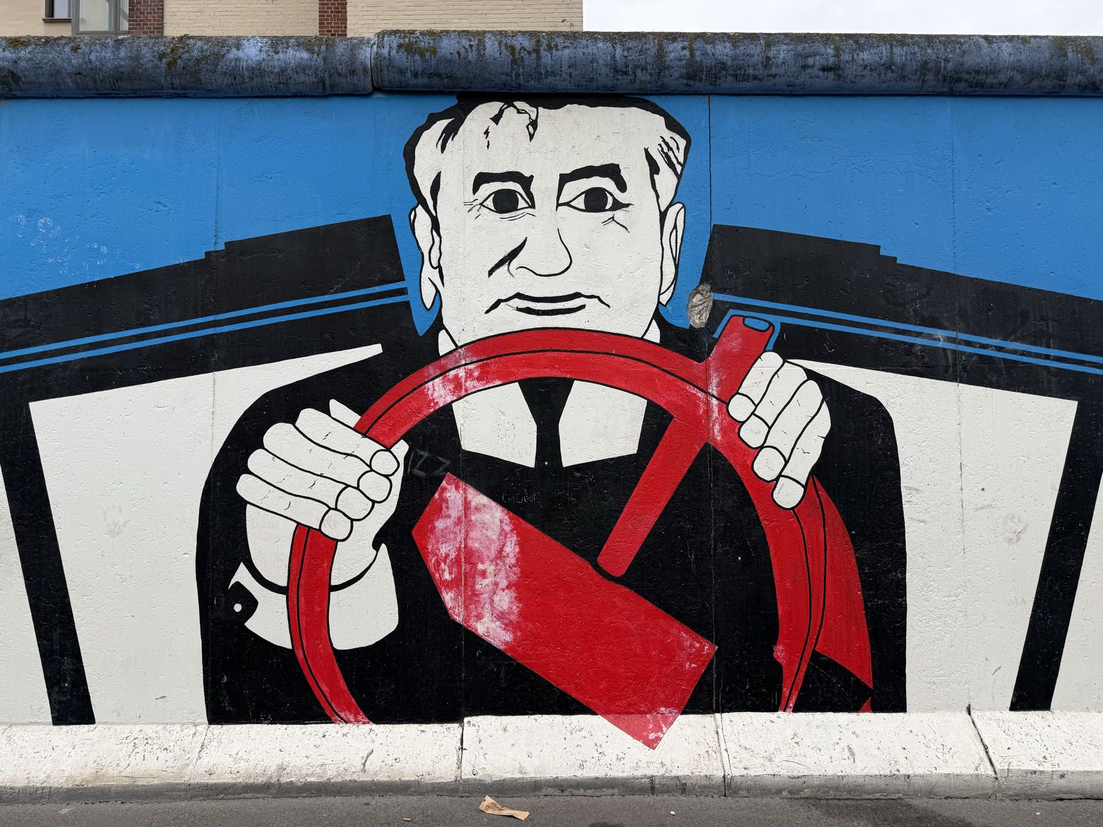 A man appears to be holding a hammer and sickle as if it were the steering wheel of a car.
