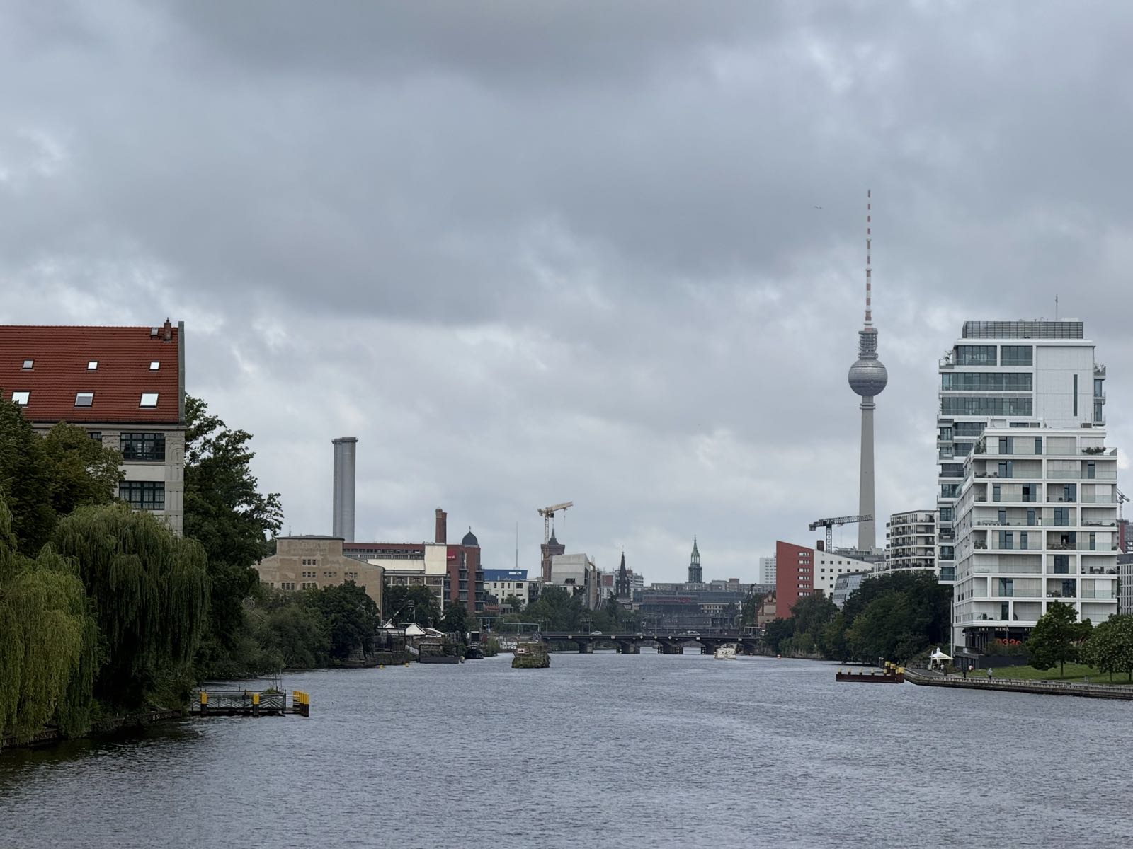 A river in a city on a cloudy day. A tall TV tower with a globe about halfway up it stands on the right. Various buildings stand on both sides of the river.