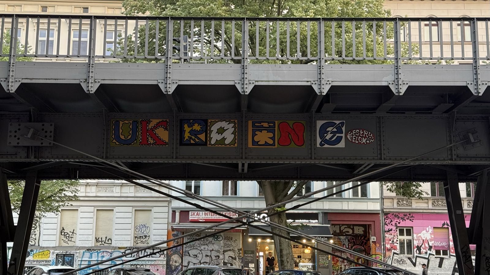 Street art reading “Ukraine” is painted on the supporting understructure of elevated train tracks. The final “e” is the old Microsoft Internet Explorer logo.