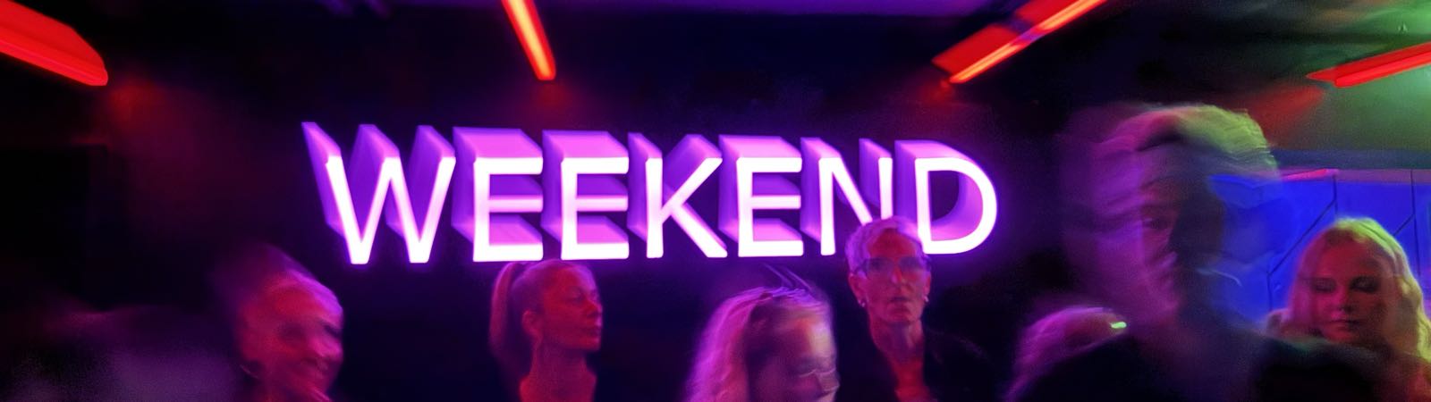 A bright pink neon sign reads “WEEKEND”. The photo is blurry, so the sign appears to come off the wall in an interesting, almost kinetic way.