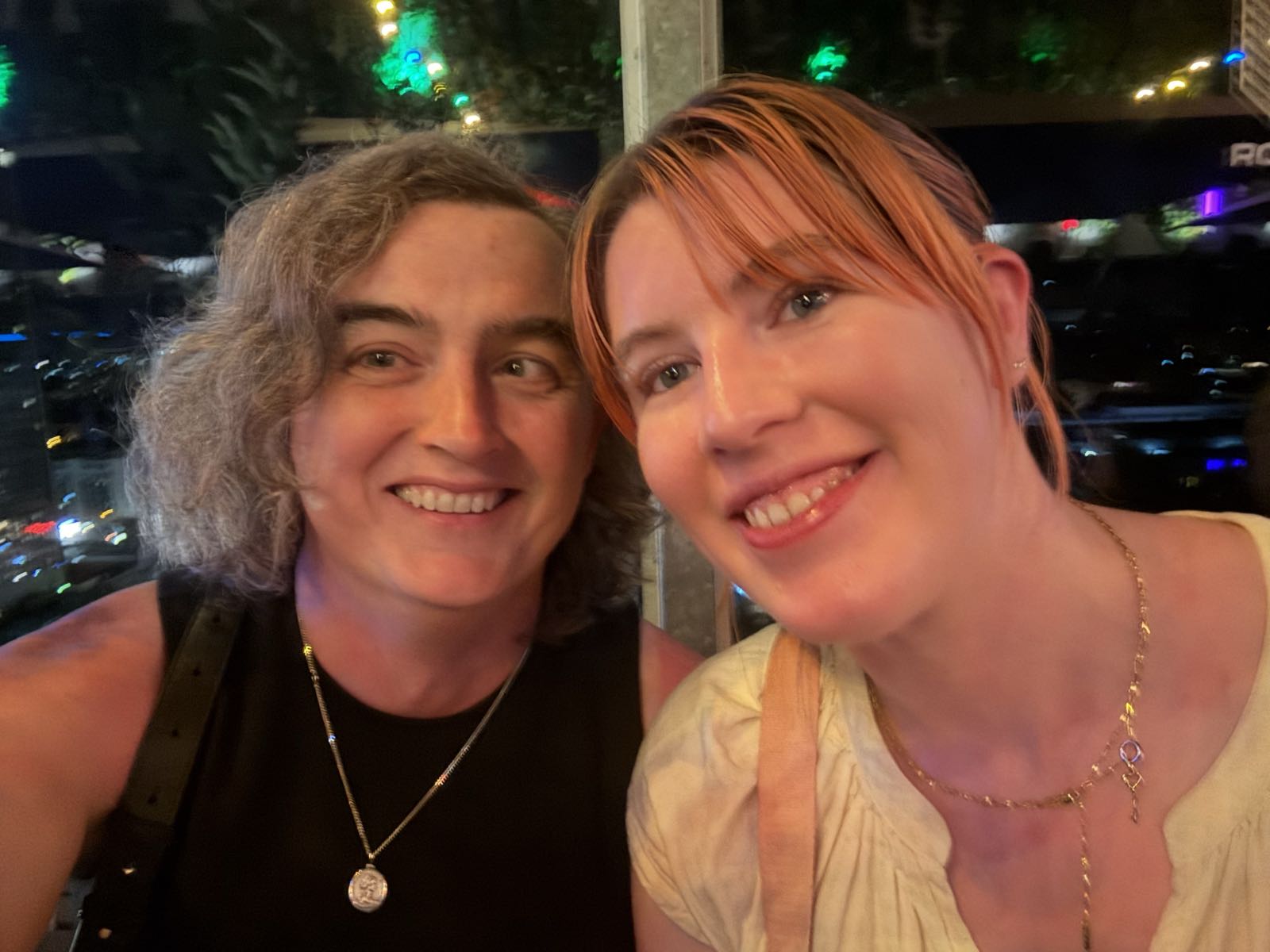 Two women smile at the camera. The one on the left is wearing a black dress, and the one on the right is in a yellow one.