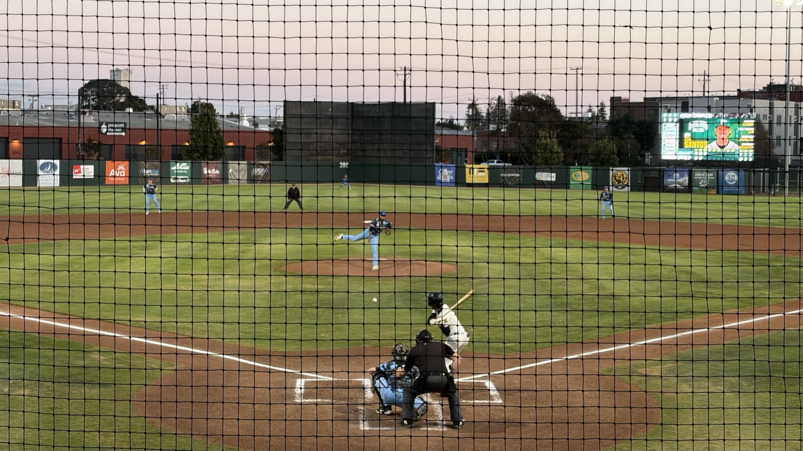 A photo of a baseball game from behind home plate. The batter is about to swing at a pitch which is mid-flight.