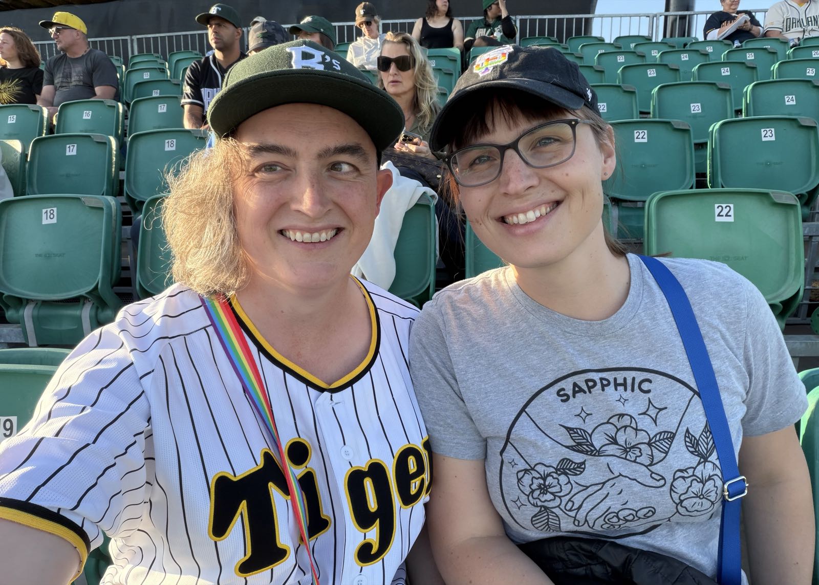A selfie of two women sitting in green seats at a stadium. They’re both smiling and wearing baseball paraphernalia.